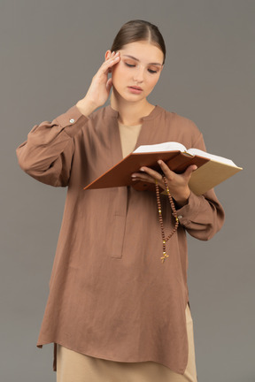 Young woman touching her temple while reading book