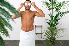 Man with towel around his waist covering his eyes with cotton pads