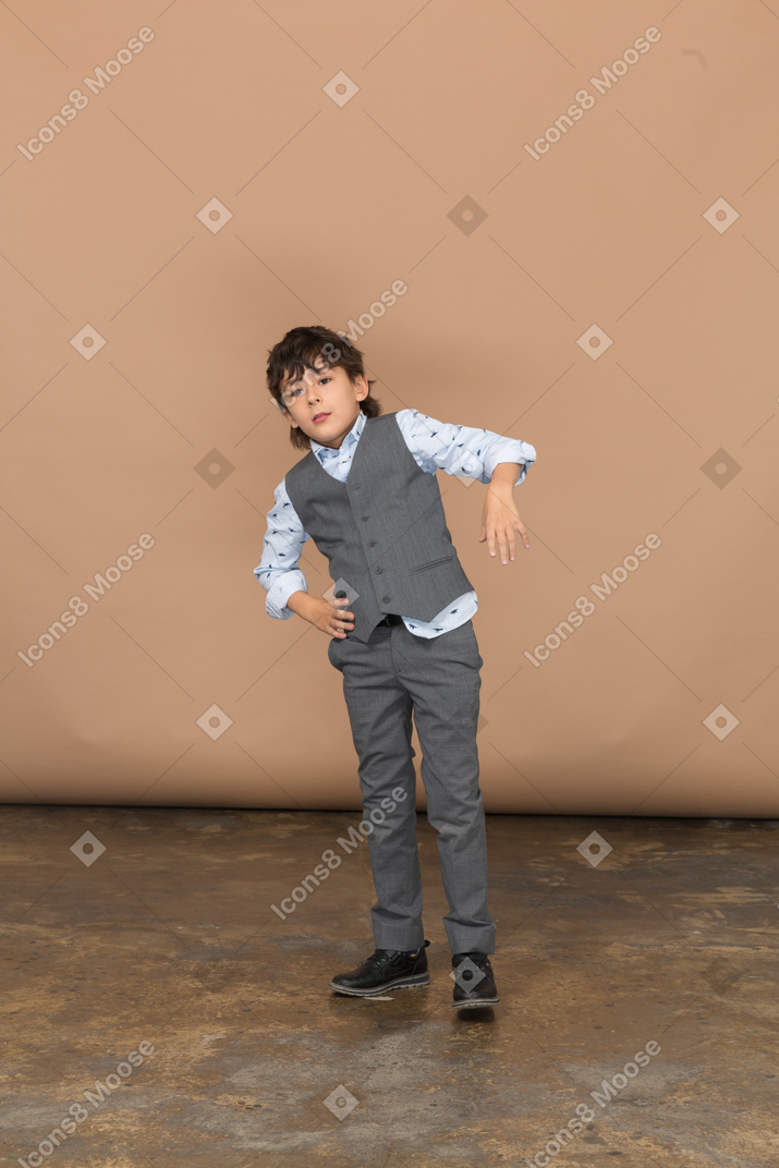 Vista frontal de un niño con traje gris de pie con las manos en las caderas
