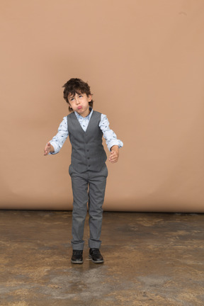 Вид спереди на симпатичного мальчика в сером костюме, корчащего рожи и жестикулирующего