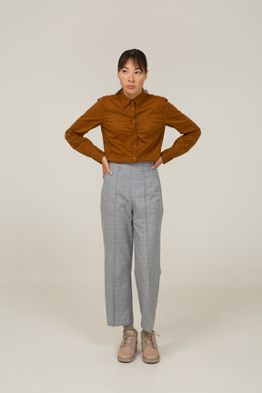 Vista frontale di una giovane donna asiatica in calzoni e camicetta che mette le mani sui fianchi