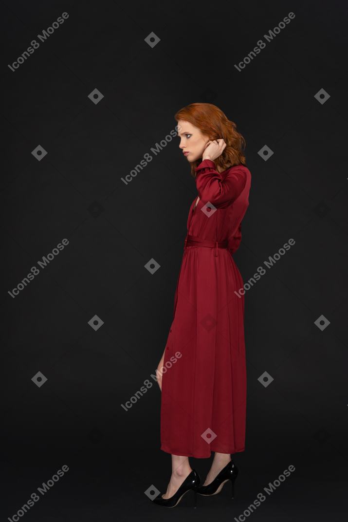 Vista lateral da jovem vestida de vermelho e tocando o cabelo