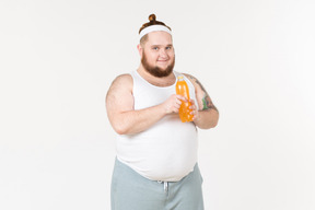 Um homem gordo no sportswear segurando uma garrafa de bebida de laranja