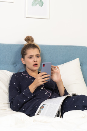 Close-up of a shocked young female in pajama lying in bed while surfing the net