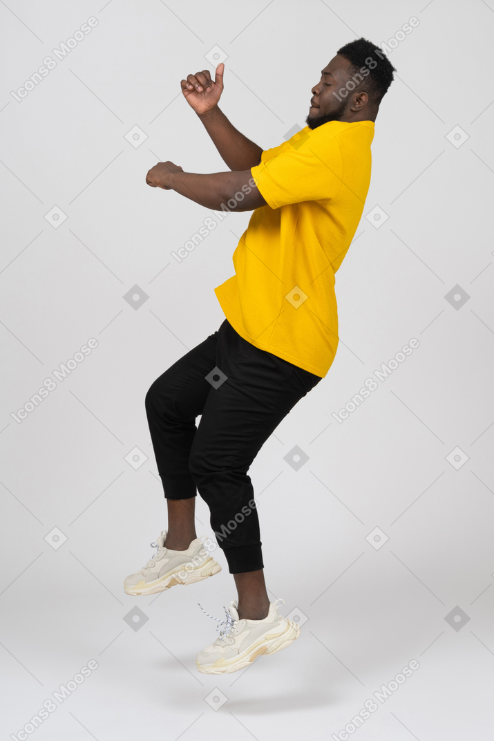 Vista lateral de un joven de piel oscura con camiseta amarilla saltando hacia atrás