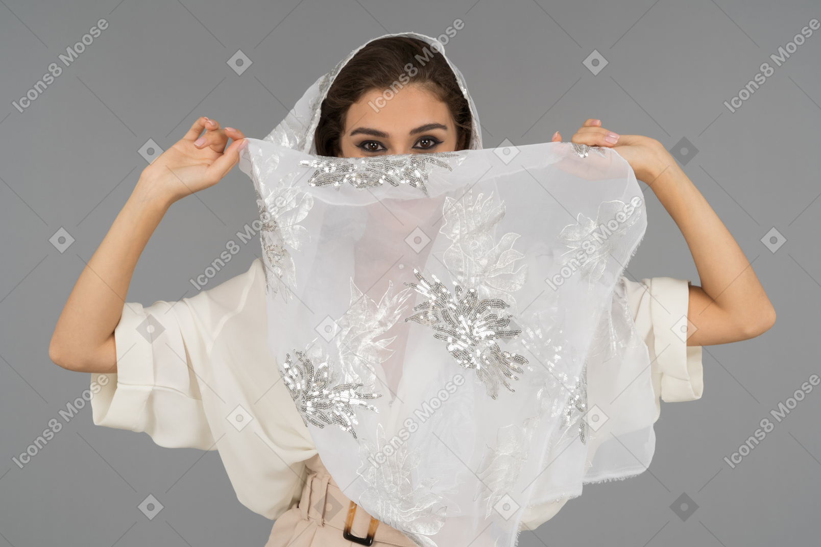 Cheerful young arab woman covering face with white shawl with silver embroidery