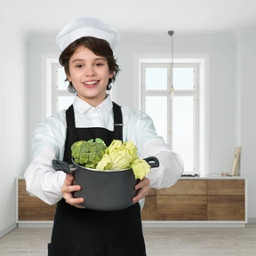 Little boy in a chef's uniform holding a pot with vegetables