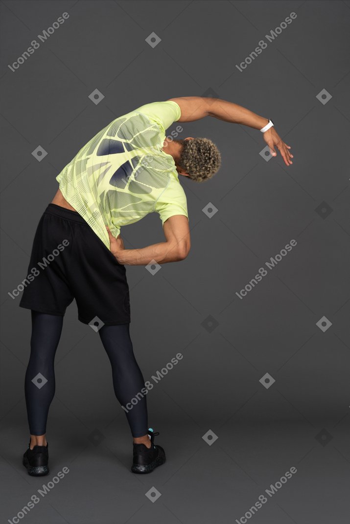 Bak view of sporty dark skinned man doing side bends