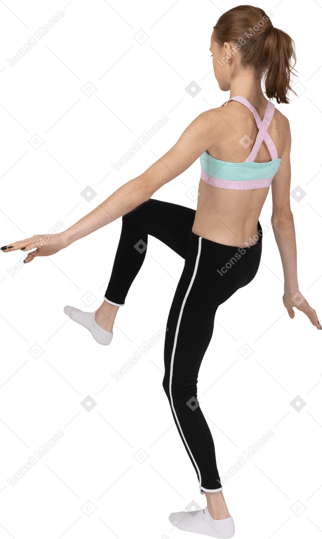 Vista posterior de tres cuartos de una jovencita en ropa deportiva extendiendo las manos y levantando la pierna