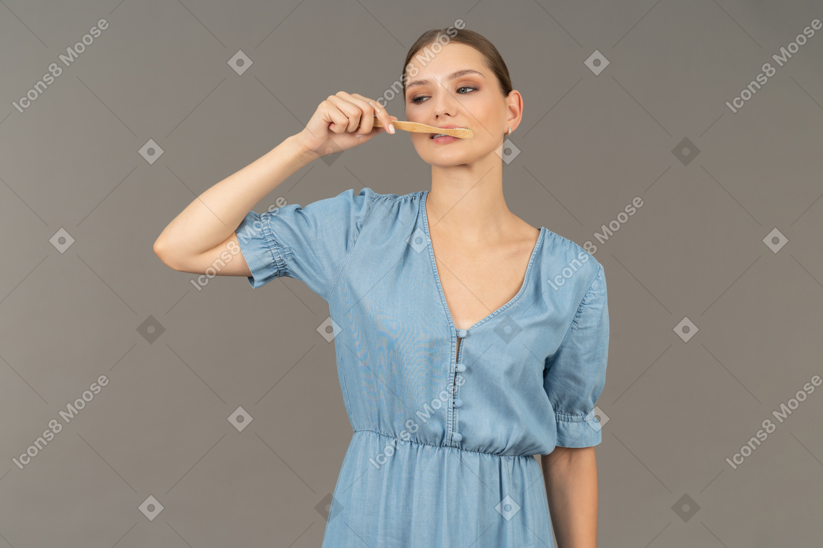 Вид спереди молодой женщины в синем платье, чистящей зубы