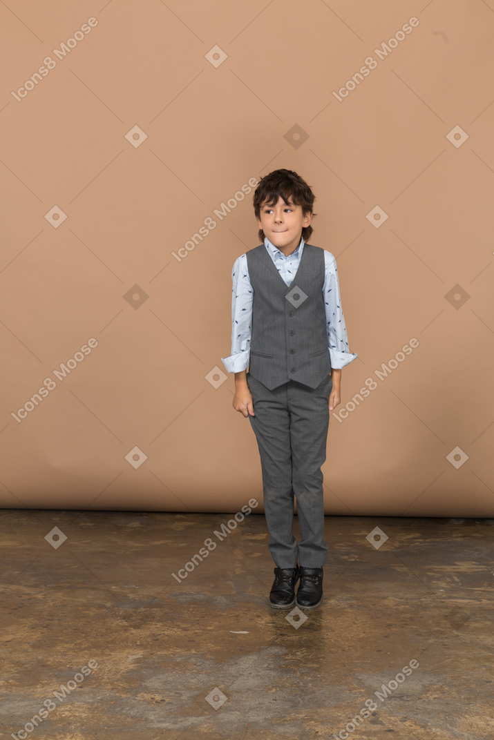 Вид спереди на симпатичного мальчика в костюме, кусающего губы