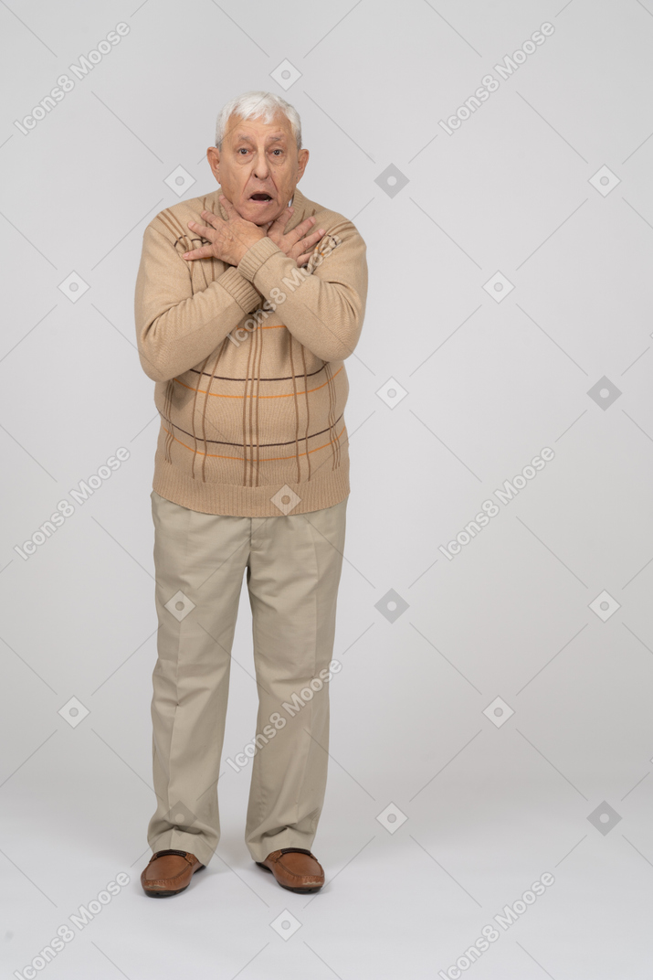 Front view of a scared old man in casual clothes standing with hands on shoulders