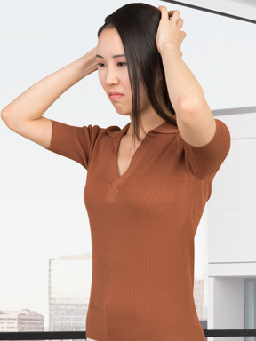 A woman in a brown shirt is holding her hair