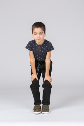 Vista frontal de un chico lindo en cuclillas y tocando las rodillas