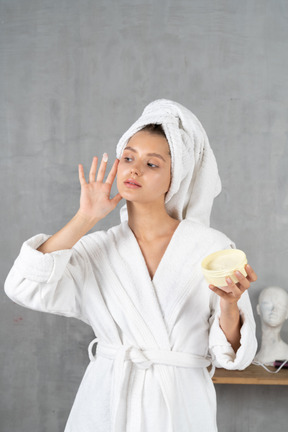 Woman in bathrobe applying face cream