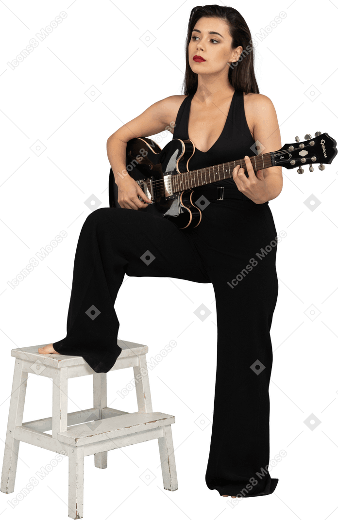 Three-quarter view of a young lady in black suit holding the guitar and putting leg on stool
