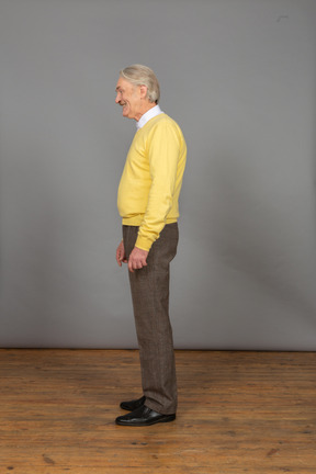 Vista lateral de un anciano feliz sonriente en un jersey amarillo mirando a un lado