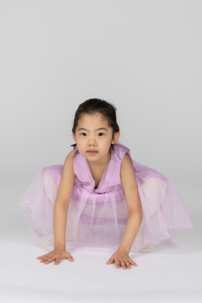 Fille en robe rose accroupie avec ses mains sur le sol