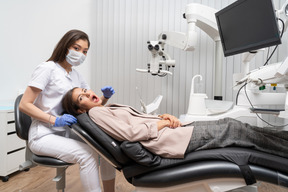 Женщина-дантист в полный рост смотрит в камеру во время осмотра своей пациентки