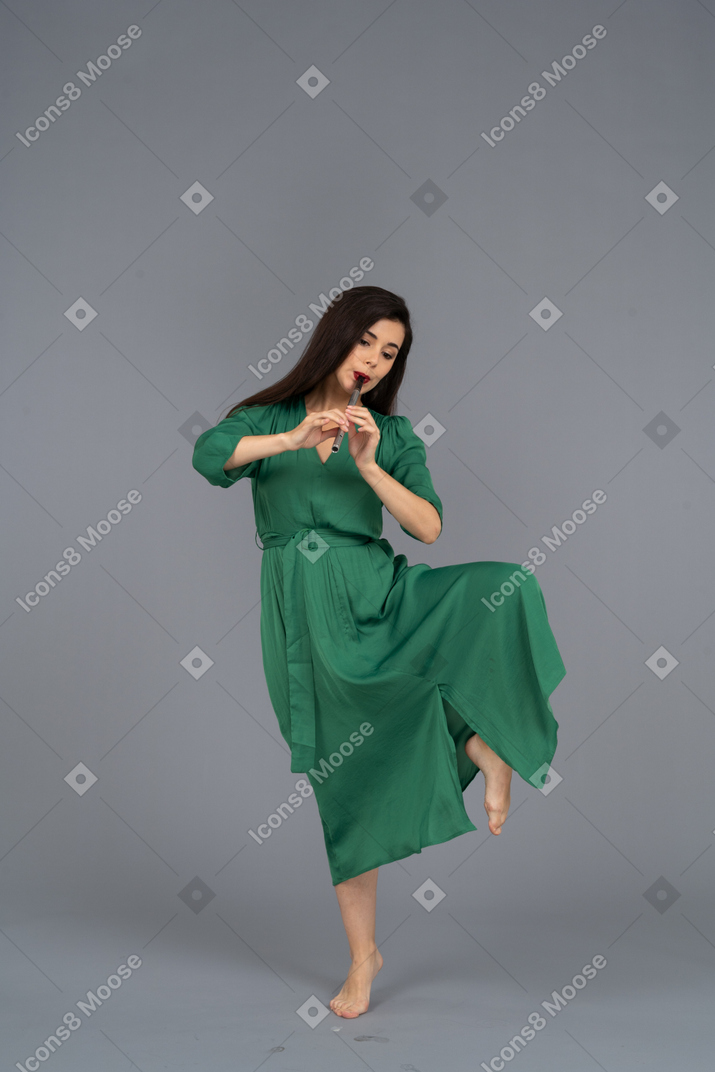 Vorderansicht einer tanzenden jungen dame im grünen kleid, das flöte spielt