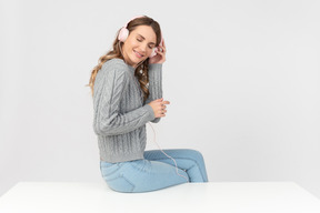 Mujer joven sentada en la mesa y escuchando música en auriculares