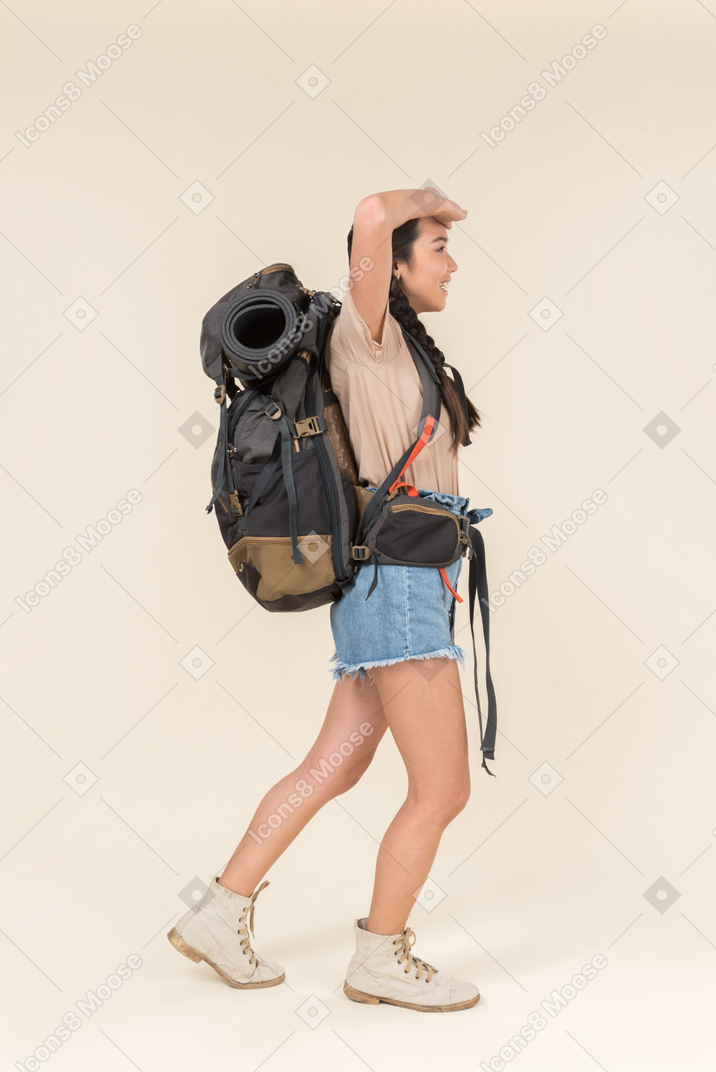 Asombrado joven excursionista asiático de pie en el perfil con una mochila enorme