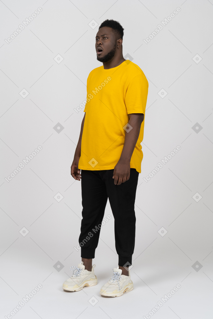 Vista di tre quarti di un giovane uomo dalla pelle scura stupito in maglietta gialla che sta fermo