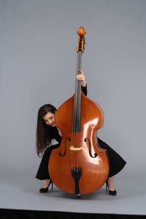 Front view of a crazy young lady squatting behind her double-bass