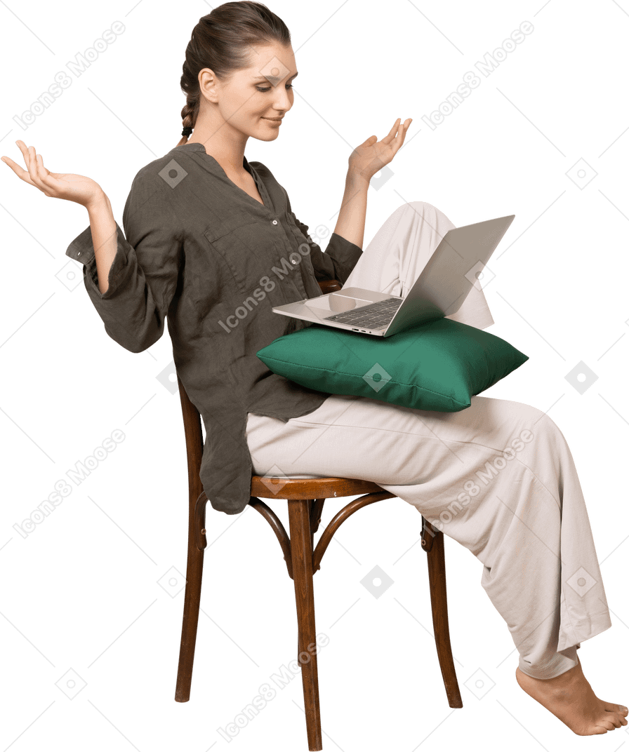 Three-quarter view of a young woman wearing home clothes sitting on a chair with a laptop & raising hands
