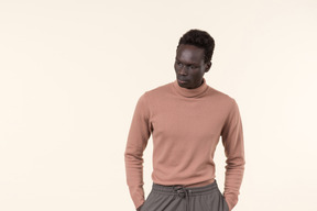 A young black man in a beige turtleneck and grey sweatpants standing casually on the white background