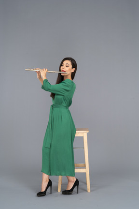 De cuerpo entero de una señorita vestida de verde sentada en una silla mientras toca el clarinete