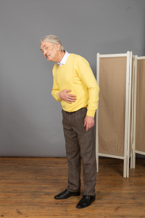 Vista de três quartos de um homem idoso colocando a mão na barriga enquanto se inclina para a frente