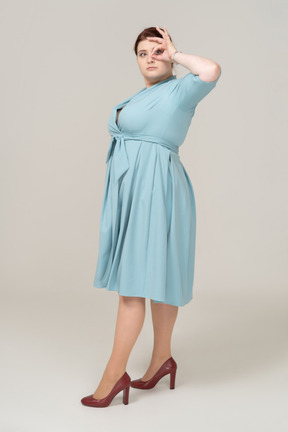 Вид сбоку на женщину в синем платье, смотрящую сквозь пальцы