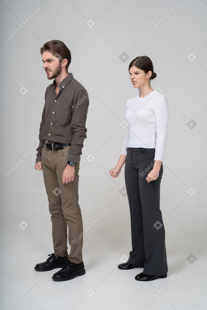 Vista de tres cuartos de una pareja furiosa en ropa de oficina apretando los puños