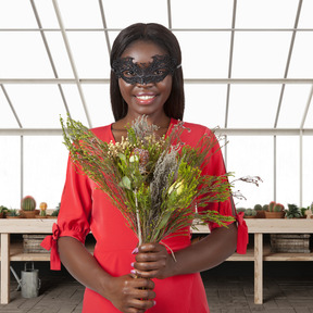 A woman wearing a masquerade mask holding a bouquet of flowers