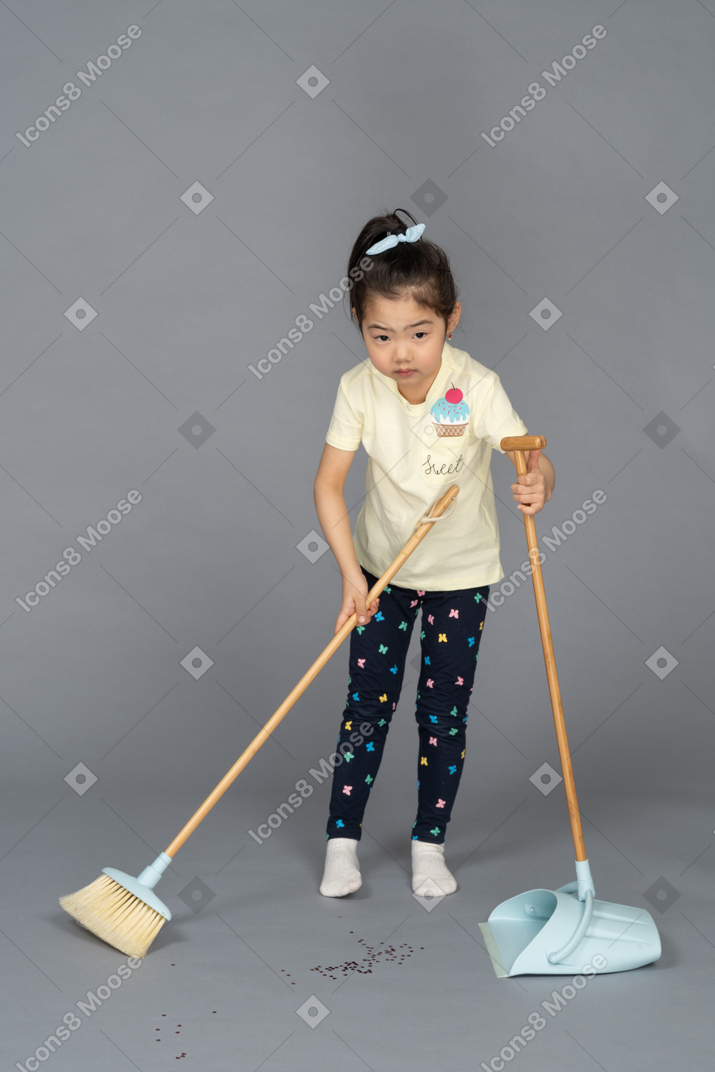 Bambina che alza lo sguardo mentre spazza il pavimento