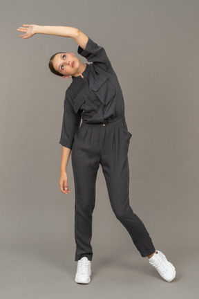 Front view of a young woman in a jumpsuit raising hand