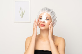 Portrait of young woman with nose bandage touching her face