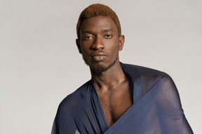 Vista frontal de un joven afro con un chal sobre los hombros mirando a la cámara