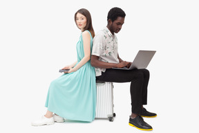 Interracial couple sitting on suitcase and and using gadjets