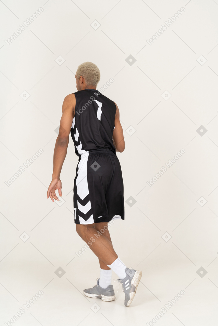 Vista traseira a três quartos de um jovem jogador de basquete confuso fazendo uma finta