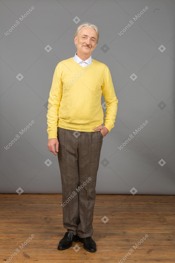 一个高兴的老人，穿着黄色套头衫，将手放在口袋里，看着相机的前视图