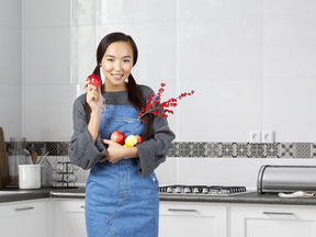 A woman standing in a kitchen holding apples