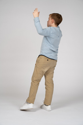Vista traseira de um menino de camisa azul, segurando as mãos para cima