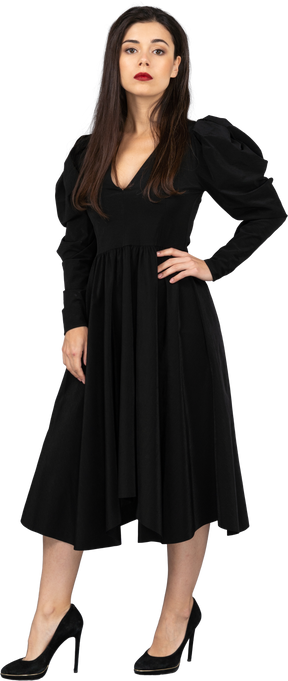 Vue de trois quarts d'une jeune femme dans une robe noire mettant la main sur la hanche