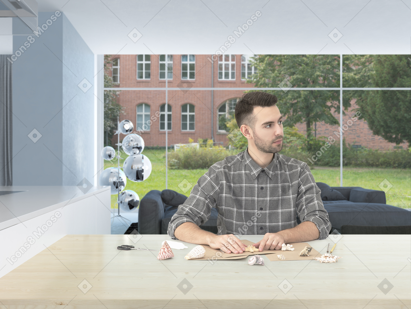 Handsome young man in a checkered shirt, sitting in a bright modern room crafting something from craft paper and seashells
