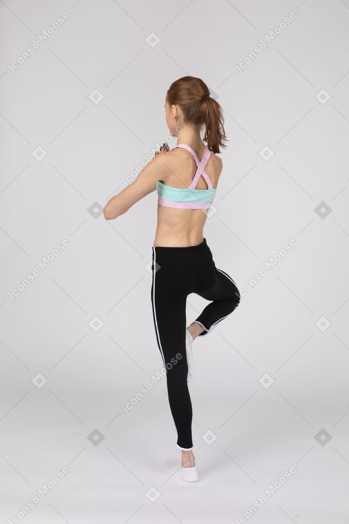 Vista posterior de tres cuartos de una jovencita en ropa deportiva en equilibrio sobre una pierna y tomados de la mano juntos
