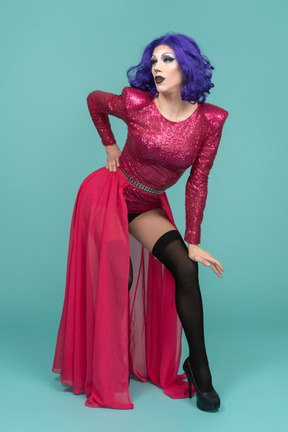 Portrait of a drag queen in pink dress posing with arched back and hand resting on knee