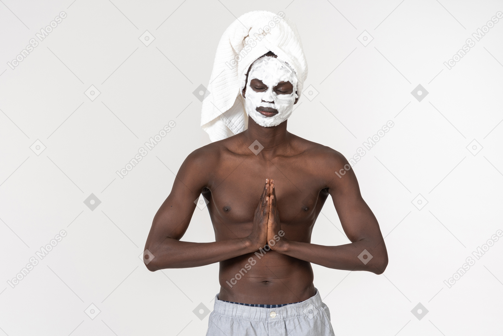 A young black man in grey trousers and a towel on his head going about his skin care routine