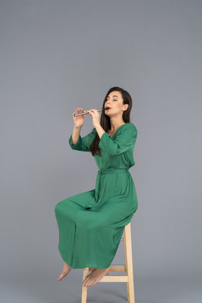 Pleine longueur d'une jeune femme en robe verte assise sur une chaise tout en jouant de la clarinette